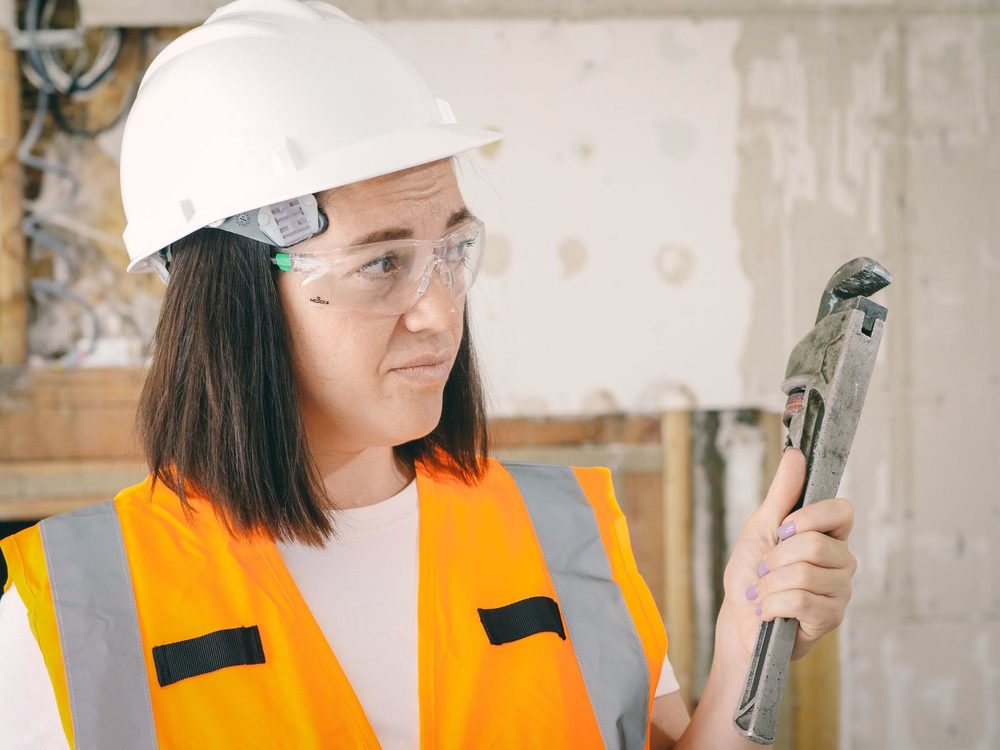 A plumber in a hard hat holding a pipe wrench inside a home